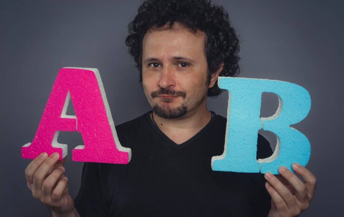 A person holds large, colorful letters A in pink and B in blue against a dark background, showcasing a playful choice between the two.