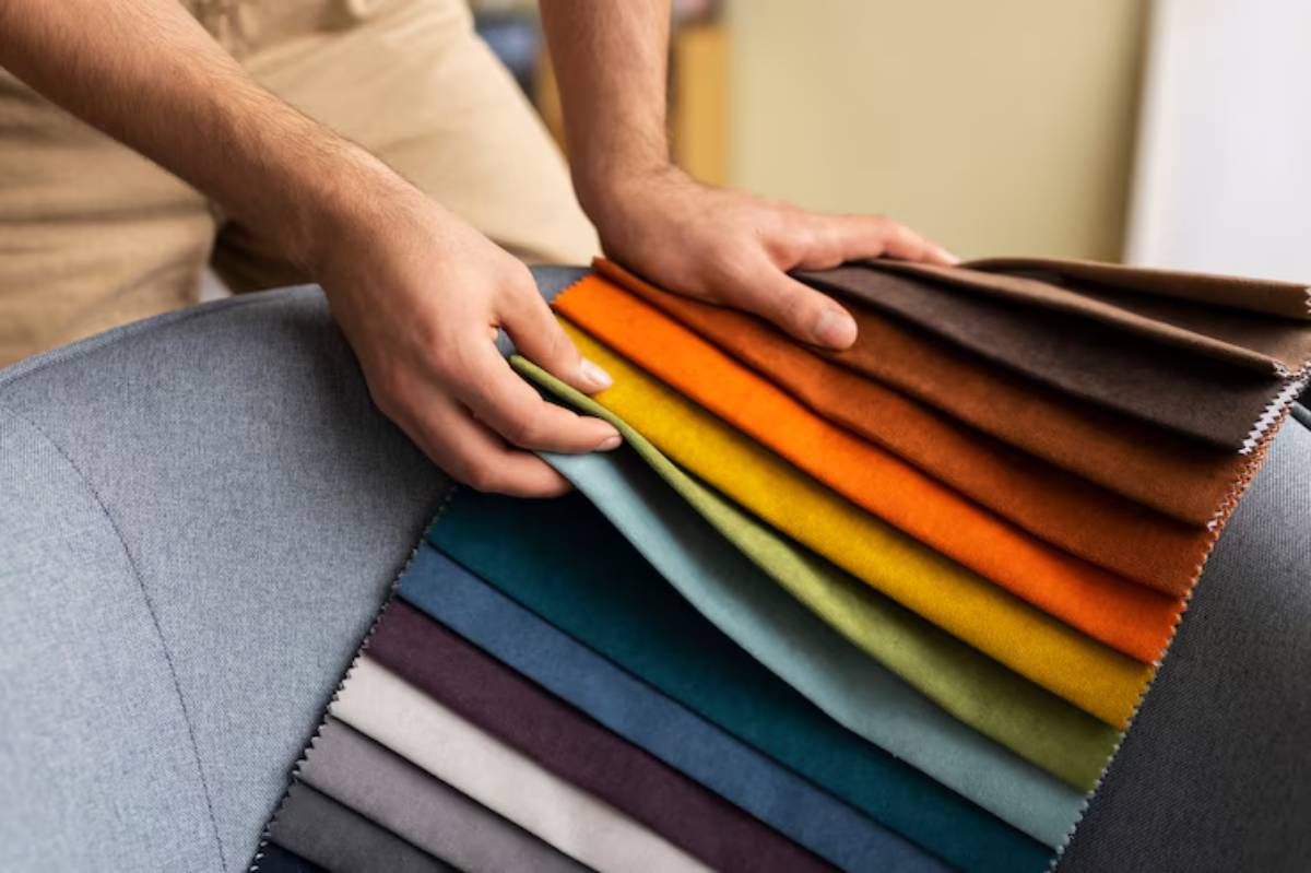 A person’s hands select from a colorful array of fabric swatches draped over a stylish gray upholstered chair.