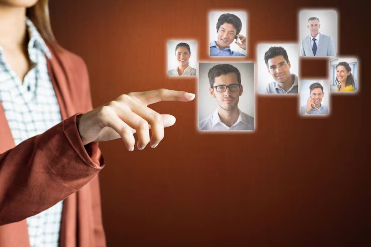 A person points at a display of nine illuminated profiles against a warm background, suggesting selection or interaction.