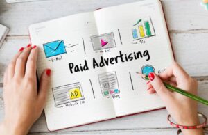 A hand with red nails writes in a notebook titled Paid Advertising, featuring sketches of email, video, ROI, website, and blog concepts.