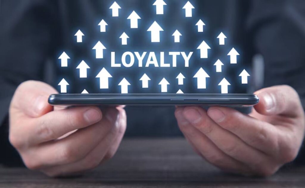 A person holding a smartphone displays the word LOYALTY with several upward-facing arrows, symbolizing growth and engagement.