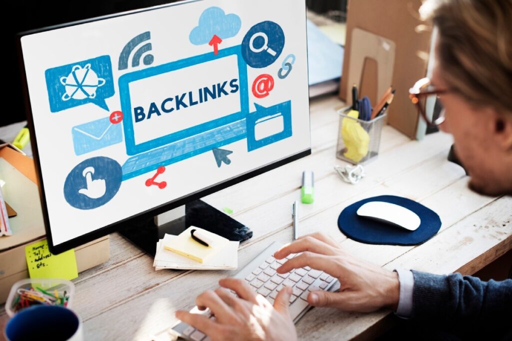 A person typing on a keyboard in front of a computer screen displaying the word BACKLINKS surrounded by various digital icons.