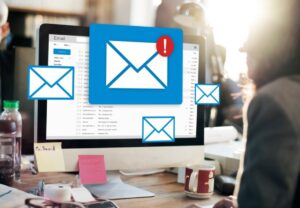 A person working at a desk with a computer displaying an email inbox and alert icons for new messages.