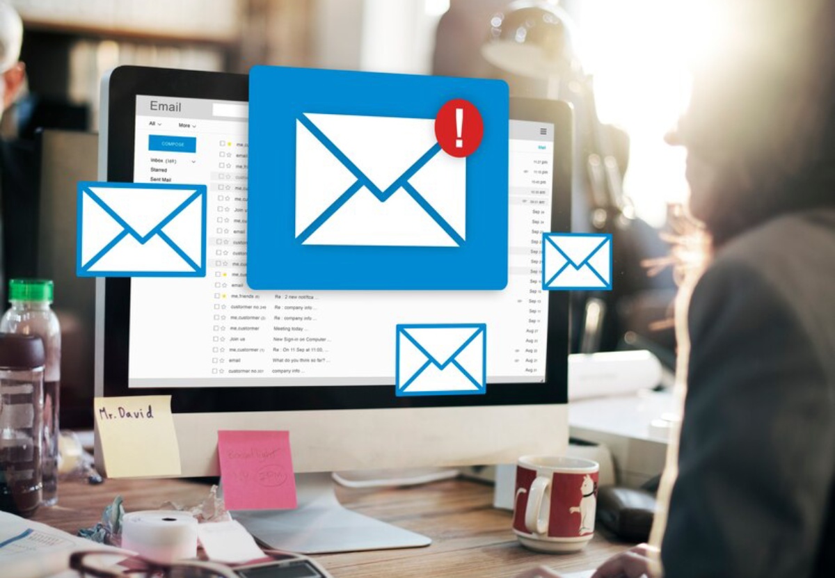 A person working at a desk with a computer displaying an email inbox and alert icons for new messages.