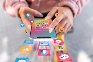 A person holding a smartphone with social media app icons and emoji reactions emerging, showcasing digital interaction and connectivity.