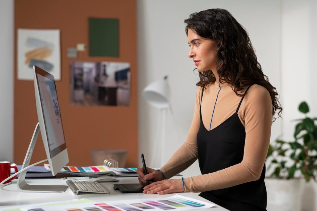 A person working on a graphic design project at a modern desk, surrounded by color swatches and a computer setup.