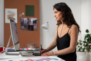 A person working on a graphic design project at a modern desk, surrounded by color swatches and a computer setup.