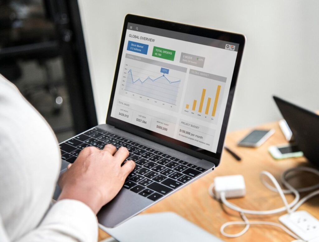 A person analyzing a financial dashboard on a laptop, showing sales data and graphs in a modern workspace.