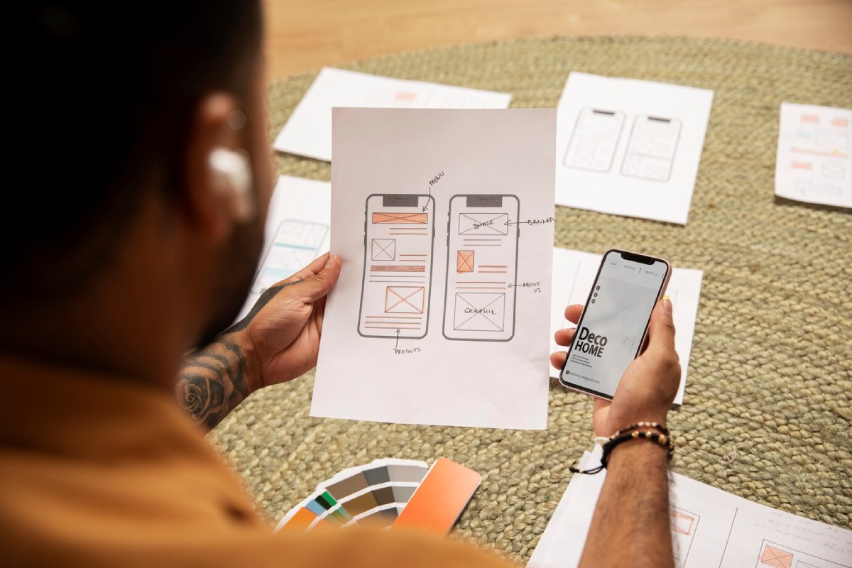 A designer reviews wireframe sketches and a mobile app mockup for 