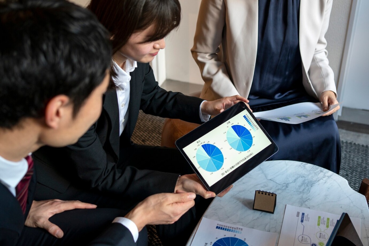 A group of professionals reviews graphs and data on a tablet during a meeting at a stylish office setting.